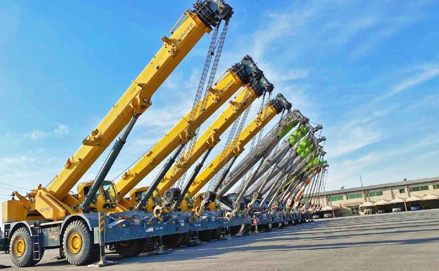 A row of yellow and green rough terrain cranes with booms raised